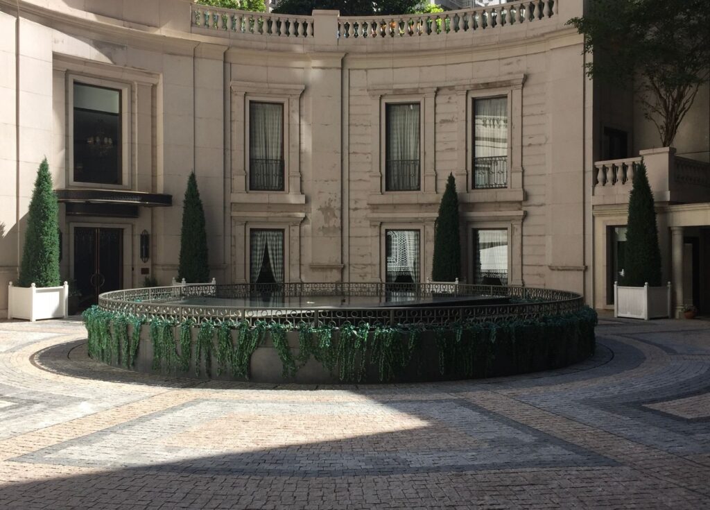 A classical stone courtyard with a circular fountain and clipped topiary
